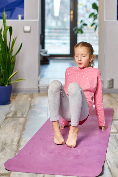 Klein meisje doen stretching oefeningen, yoga oefenen op fitness mat thuis, Sporten, Gezonde levensstijl. Kinderen sport home quarantaine - Foto, afbeelding