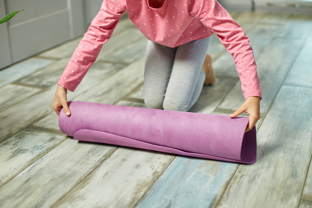 Gyermek, kislány felgördül jóga pilates szőnyeg a földön nyújtás után gyakorlatok, jóga gyakorlása, sportolás, egészséges életmód. - Fotó, kép