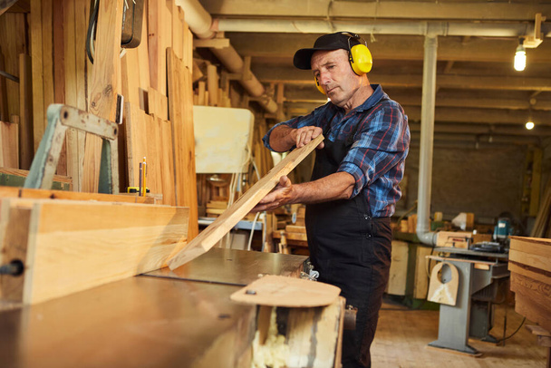 Старший плотник в униформе работает на деревообрабатывающей машине в столярном производстве - Фото, изображение