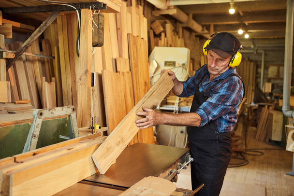 Senior tesař v uniformě pracuje na dřevoobráběcím stroji v tesařské výrobě - Fotografie, Obrázek