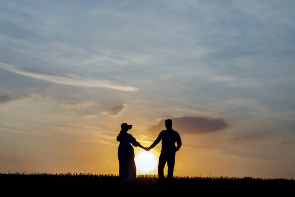 Silhouetten eines jungen Paares am Horizont, im Hintergrund geht die Sonne unter - Foto, Bild