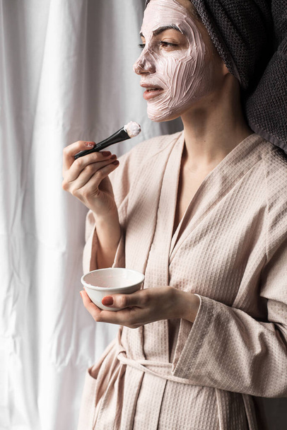 beautiful young woman with facial mask on her face and bathrobe in bathroom - Foto, afbeelding