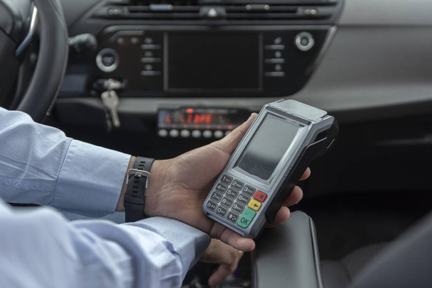 unrecognizable cab driver holding a bank payment terminal to process credit card payment purchases - transport concept, cab, taxi and technology - Photo, image
