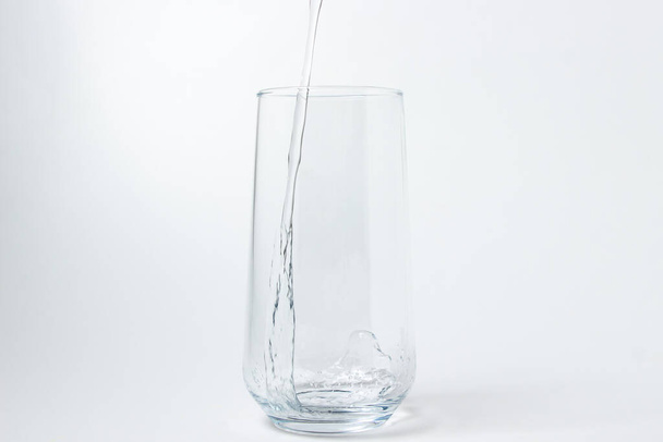 Woda pitna jest wlewana do szklanki na białym tle. Czysta woda pitna. Ugaszacz pragnienia - Zdjęcie, obraz