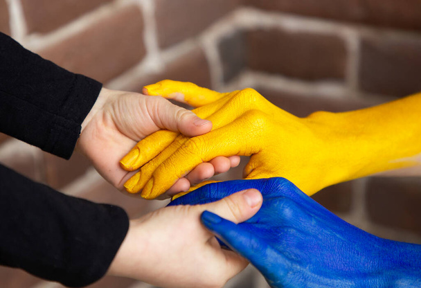 children's small hands hold female hands painted in yellow and blue colors of Ukrainian flag. Family together, peace, care. Support Ukrainians during the war on territory of Ukraine. Selective focus - Photo, image