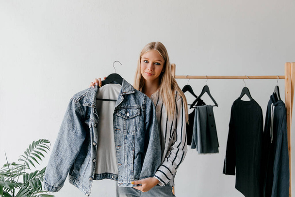 Young fashion vlogger trying on blue denim jacket, showing it on a hanger - Photo, Image