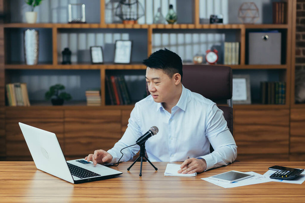 Asian freelancer records audio podcasts, businessman works in office, uses professional microphone and laptop - 写真・画像