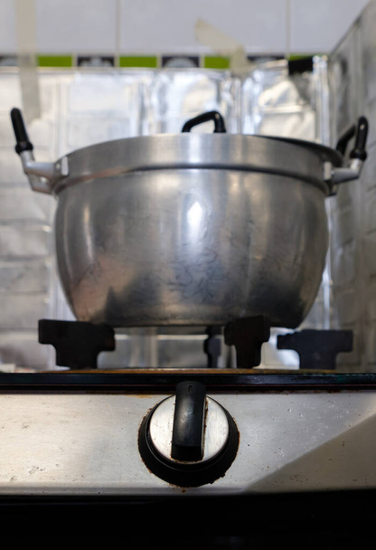 The large metal pot on the gas stove after cooking in the kitchen of the city house, selective focus on the gas stove switch, front view with the copy space. - Foto, imagen
