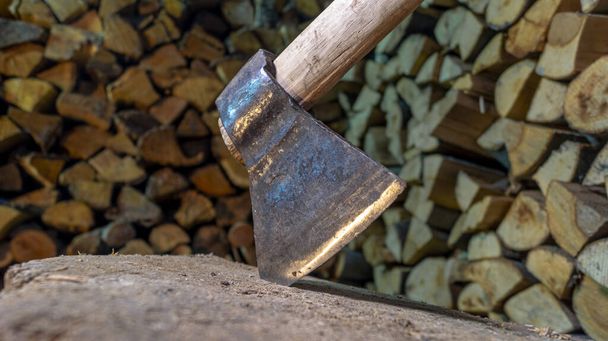 Um machado com uma alça de madeira presa em um toco para cortar lenha no celeiro contra um fundo de outra lenha - Foto, Imagem