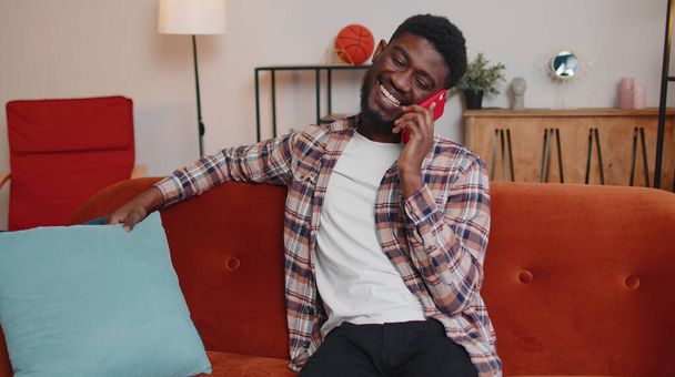 Joven adulto afroamericano hombre disfrutando hablando de teléfono móvil conversación con amigos en casa - Foto, Imagen