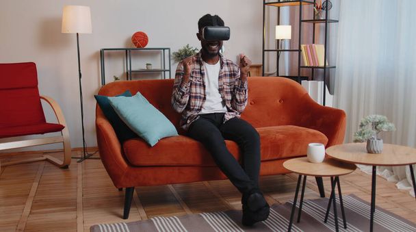 Nuori kaveri käyttää virtuaalitodellisuus kuulokkeet lasit kotona pelata 3D videopeli tekee eleitä kädet - Valokuva, kuva