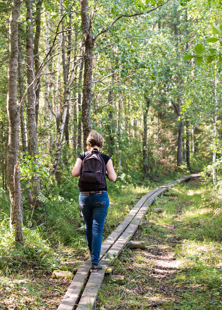 Young healthy woman with backpack walking over a wooden path in the Florarna Naturreservat , a Swedish Nature Reserve Park - Foto, Imagem