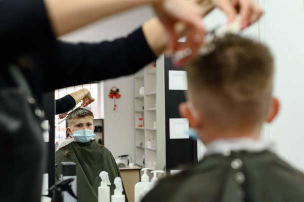 Детская стрижка в парикмахерской, стильная и современная стрижка для школьников, работа во время пандемии, вид в зеркало в парикмахерской. - Фото, изображение