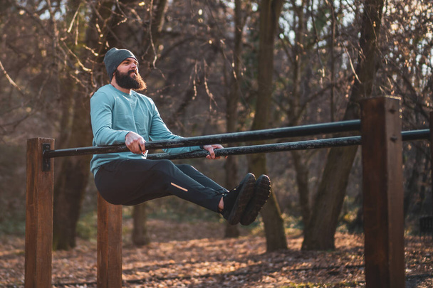 Man enjoys  exercise push- ups on parallel bars in the park. - Photo, image