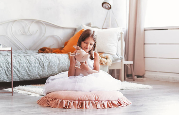 little smiling cute girl in beautiful white dress is sitting with soft toy in her hands - Fotoğraf, Görsel