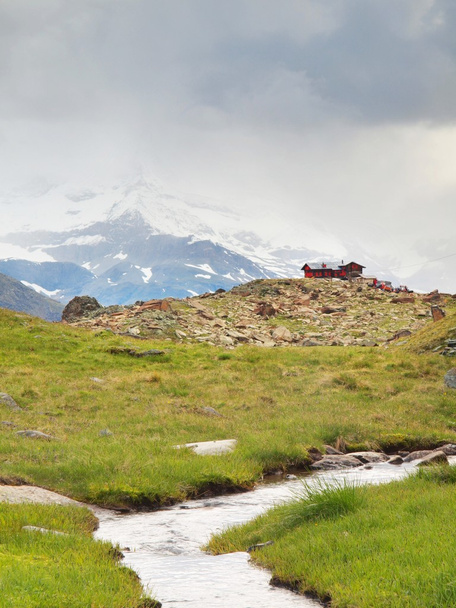 Arroyo en el prado verde fresco de los Alpes, picos nevados de los Alpes en el fondo. Clima frío brumoso y lluvioso en las montañas al final del verano
 - Foto, imagen