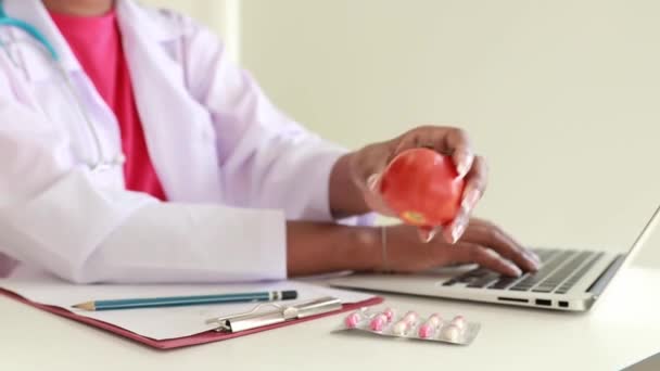 Афроамериканська дієтолог сидить на клавіатурі, щоб записати інформацію та переваги помідорів для плану дієти для пацієнтів, щоб заощадити на ноутбуці для роботи клініки.. - Кадри, відео