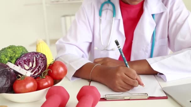 Una nutrizionista afro-americana si siede note e benefici di pomodori e broccoli per il suo piano alimentare paziente dell'ufficio ospedaliero. - Filmati, video