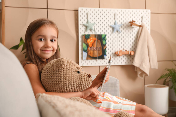 Cute little girl with teddy bear using tablet computer at home - Fotó, kép