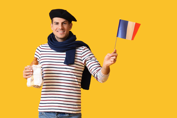 Hezký mladý muž s vlajkou Francie a croissanty na žlutém pozadí - Fotografie, Obrázek