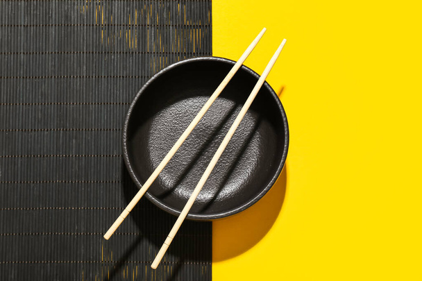 Bambusová rohožka s čínskou miskou a hůlkami na barevném pozadí - Fotografie, Obrázek