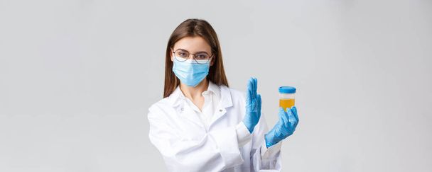 Covid-19, medical research, diagnosis, healthcare workers and quarantine concept. Doctor, intern in medical mask and gloves, lab clinic testing urine sample, show rejection and refusal gesture - Φωτογραφία, εικόνα