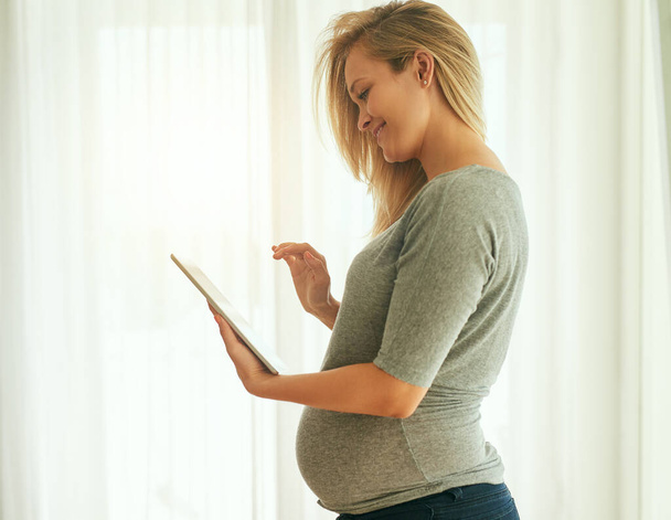 Таким чином я можу перевірити розвиток своїх малюків щотижня. Обрізаний знімок вагітної жінки, використовуючи свій цифровий планшет вдома
. - Фото, зображення