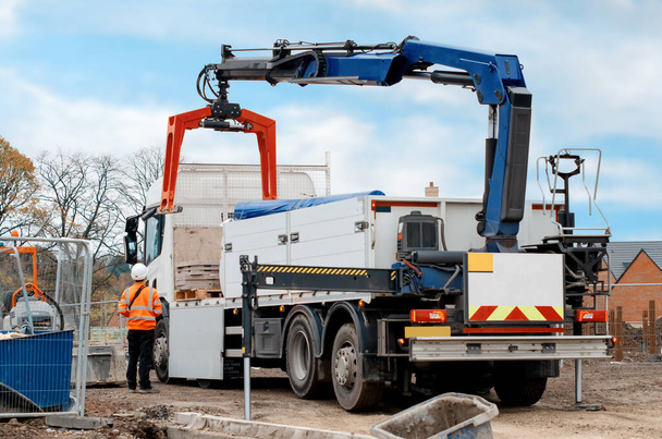 Dropside plakalı HIAB vinç kamyonu tuğla kapma eklentisiyle inşaat alanına malzeme getiriyor ve indiriyor. - Fotoğraf, Görsel