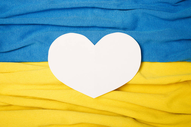 Ukraine flag background with fabric texture wave and white paper heart. - Photo, Image