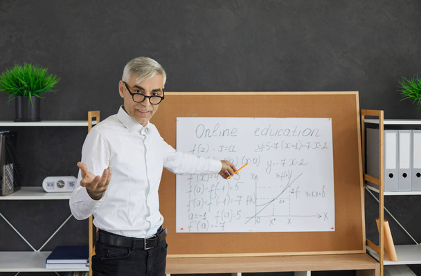 Portrait of senior teacher standing in front of classroom board during online class - Foto, afbeelding