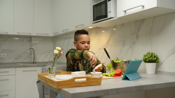 Preteen niño aprendiendo a cocinar a través de la plataforma de vídeo en línea para compartir en interiores - Metraje, vídeo