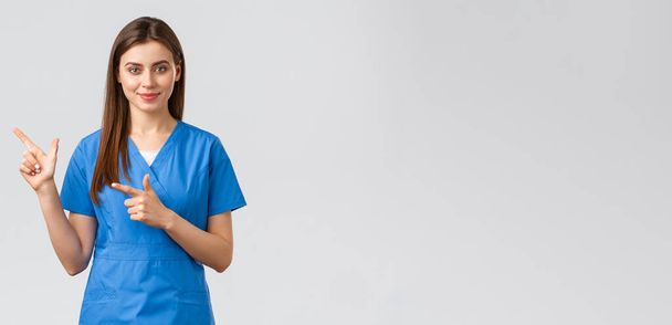 Медицинские работники, предотвратить вирус, страхование и медицина концепции. Улыбающаяся привлекательная женщина-врач или медсестра в синей форме, указывающая пальцем влево, чтобы показать пациентам рекламу, важную информацию
 - Фото, изображение