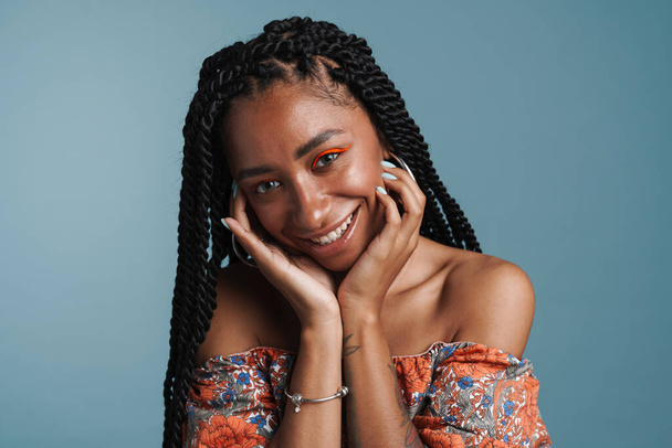Young black woman with makeup smiling and looking at camera isolated over blue background - Foto, afbeelding