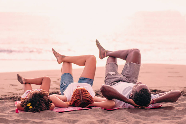 Familia joven de raza mixta relajarse en la playa. Los padres con hija disfrutando de unas vacaciones en el mar. Concepto de familia y viaje. - Foto, imagen