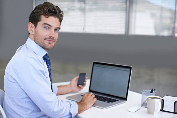 Good client communication is his priority. Portrait of a young businessman seated at his desk with a mobile phone in his hand. - Foto, imagen