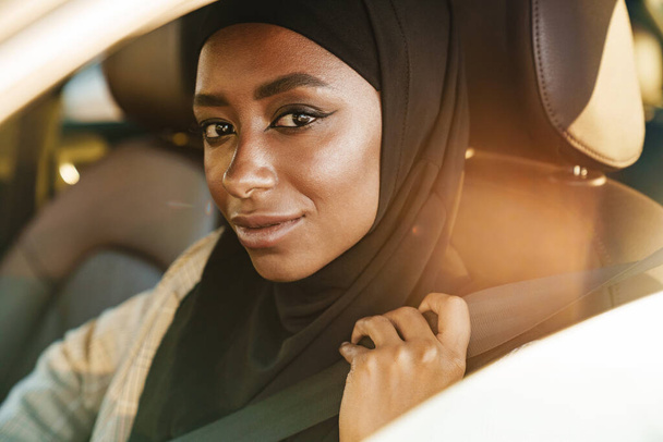 Black muslim woman wearing headscarf smiling while driving car - Zdjęcie, obraz