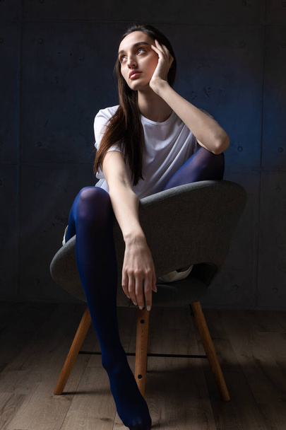 Πορτρέτο μιας νεαρής μελαχρινής με μακριά μαλλιά στο στούντιο. Δραματική φωτογραφία σε σκούρα χρώματα. - Φωτογραφία, εικόνα