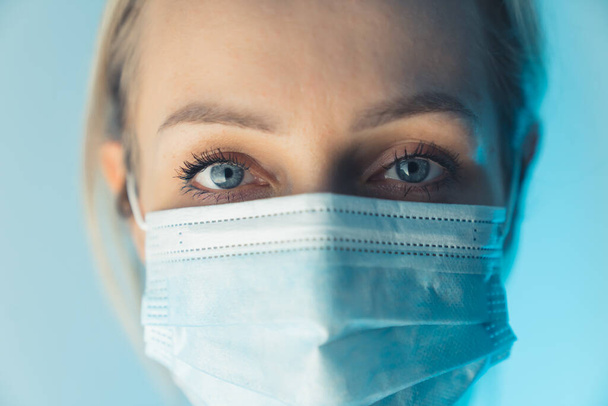 Tiredness in the eyes of European health worker. Close up studio shot caucasian woman wearing surgical mask. - Φωτογραφία, εικόνα
