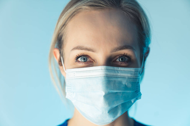 Confident caucasian nurse lady wearing professional mask, educates about safety. close up studio shot, blue background. - Foto, immagini