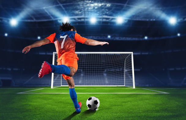 Voetbal scene in de nacht wedstrijd met speler in een oranje en blauw uniform schoppen de strafschop - Foto, afbeelding