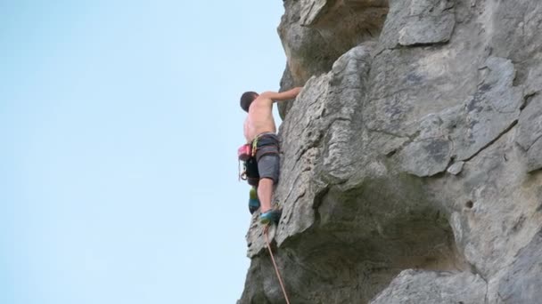 Ισχυρός αρσενικός αναρριχητής σκαρφαλώνει απότομο τοίχο βραχώδους βουνού. Ο αθλητής ξεπερνάει τη δύσκολη διαδρομή. Συμμετέχοντας σε ακραίες αθλητικές έννοια χόμπι - Πλάνα, βίντεο