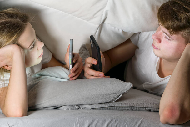 children play games on a smartphone or tablet at night under a blanket, rewrites with friends on social networks. social media addiction - Photo, Image