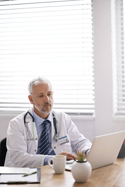 Typing out some medical reports. Cropped shot of a mature male doctor working at his desk. - Foto, imagen
