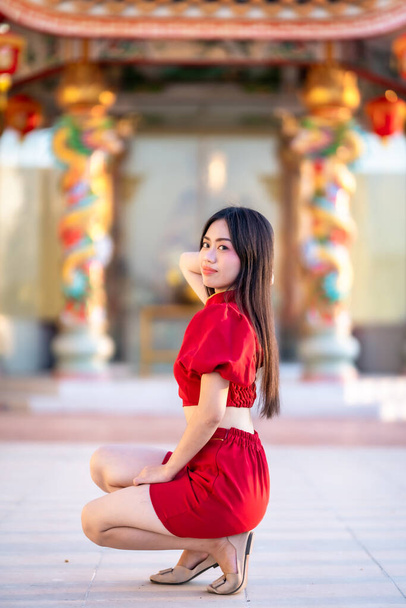 Portrait beautiful smiles Asian young woman wearing red cheongsam dress traditional decoration for Chinese new year festival celebrate culture of china at Chinese shrine Public places in Thailand - Photo, Image