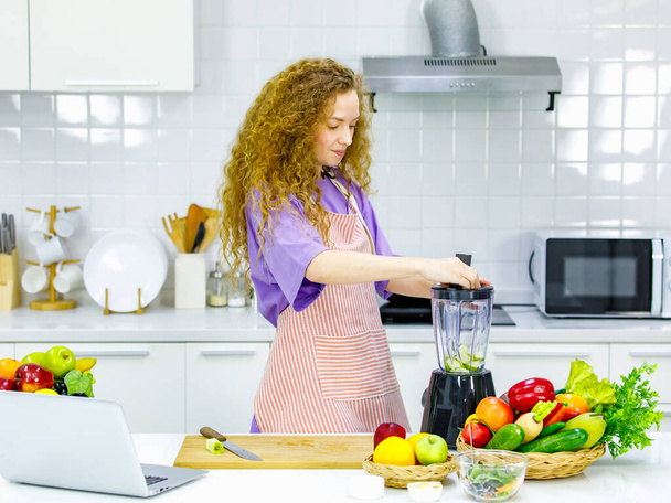 Caucasian happy pretty curly hair healthy big belly tummy pregnancy mother in apron standing learning cooking online from laptop computer holding knife cutting vegetable on wooden board in kitchen. - Foto, immagini