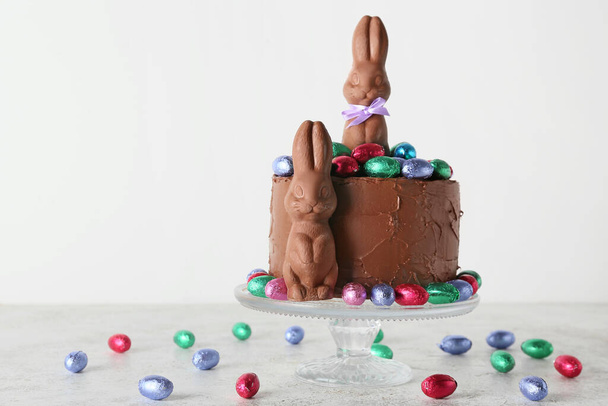Вкусный пасхальный торт, украшенный шоколадными кроликами и сладостями на светлом фоне - Фото, изображение