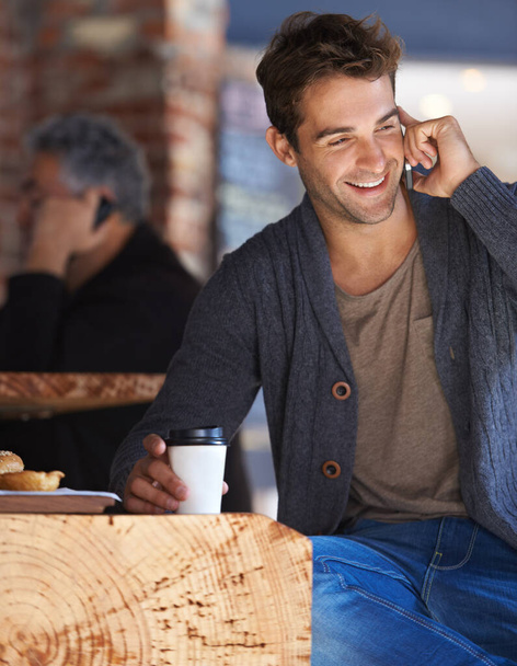 So schön, wieder von Ihnen zu hören. Aufnahme eines jungen Mannes, der in einem Café sitzt und mit einem Handy spricht. - Foto, Bild