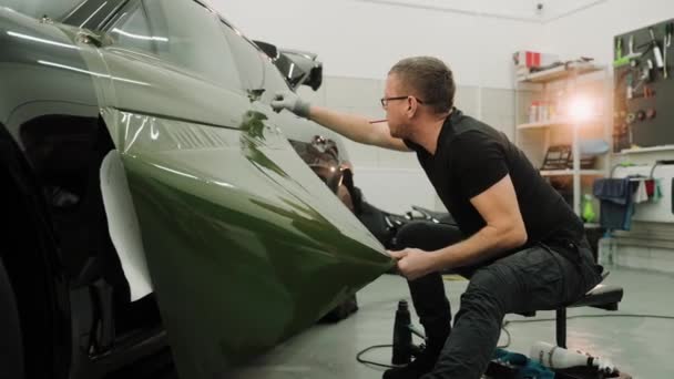 Close up shot of man vinyl wrapping the car door, pulling the film down. Process of vinyl wrapping a car using heat gun. Green vinyl film for car wrapping. High quality 4k footage - 映像、動画