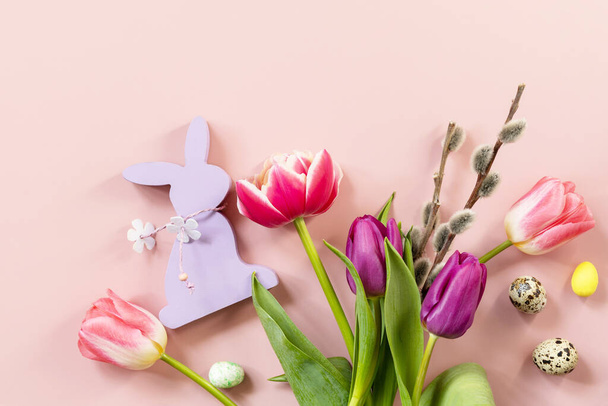 Paascompositie met kleurrijke paaseieren en lentebloemen tulpen over roze achtergrond. Voorjaars- en paasvakantie concept. Bovenaanzicht vlak. Kopieerruimte. - Foto, afbeelding