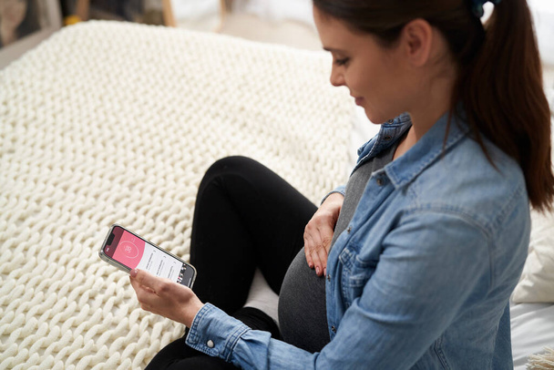 Беременная белая женщина с помощью мобильного приложения на смартфоне - Фото, изображение